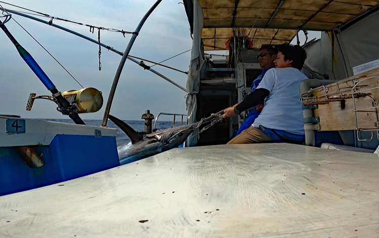 クレーンズ沖縄、鶴丸のトローリングにてカジキを船に引き上げる男性と鶴巻船長