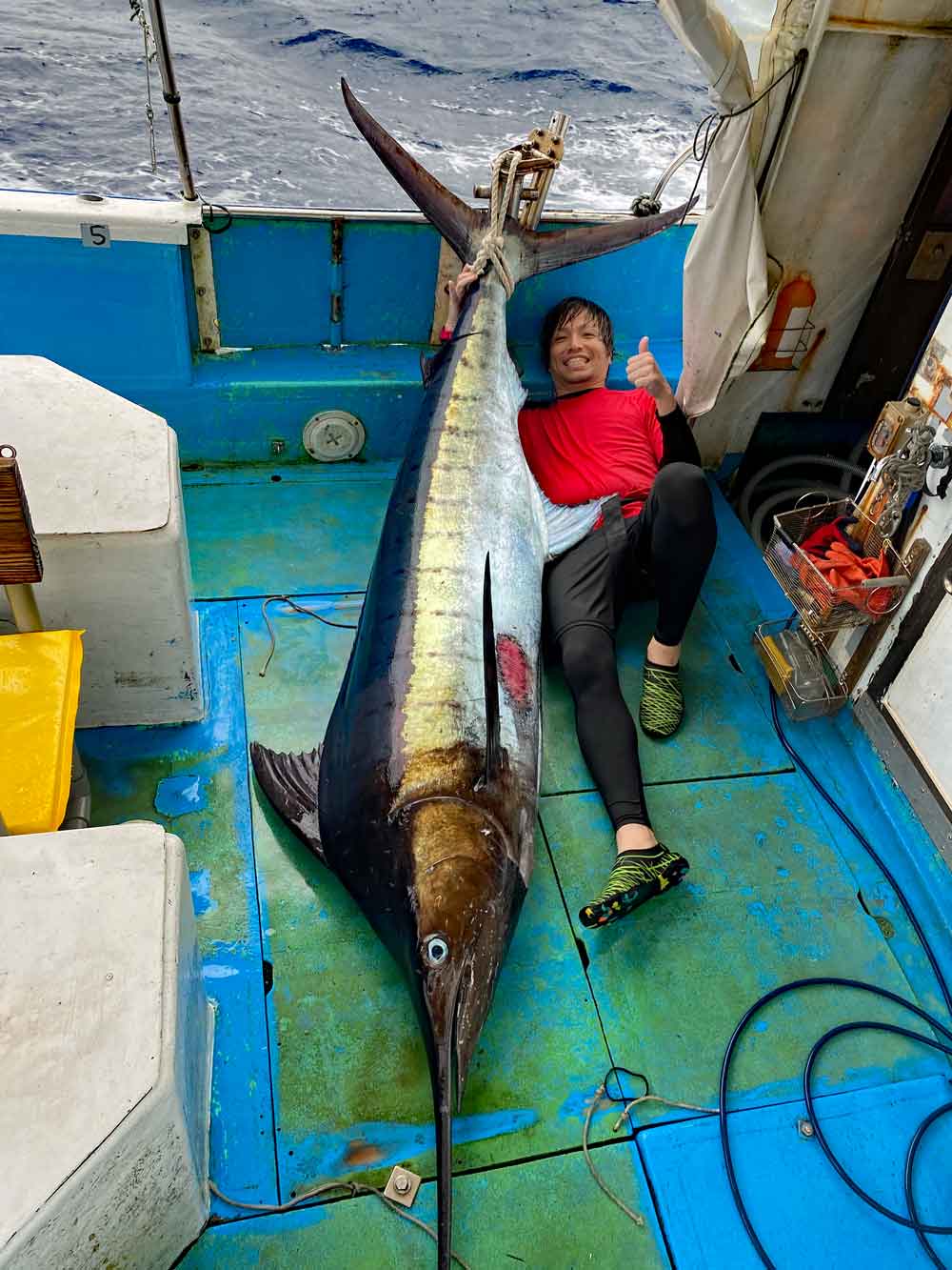 沖縄のトローリングでカジキを釣り上げた赤いシャツの男性