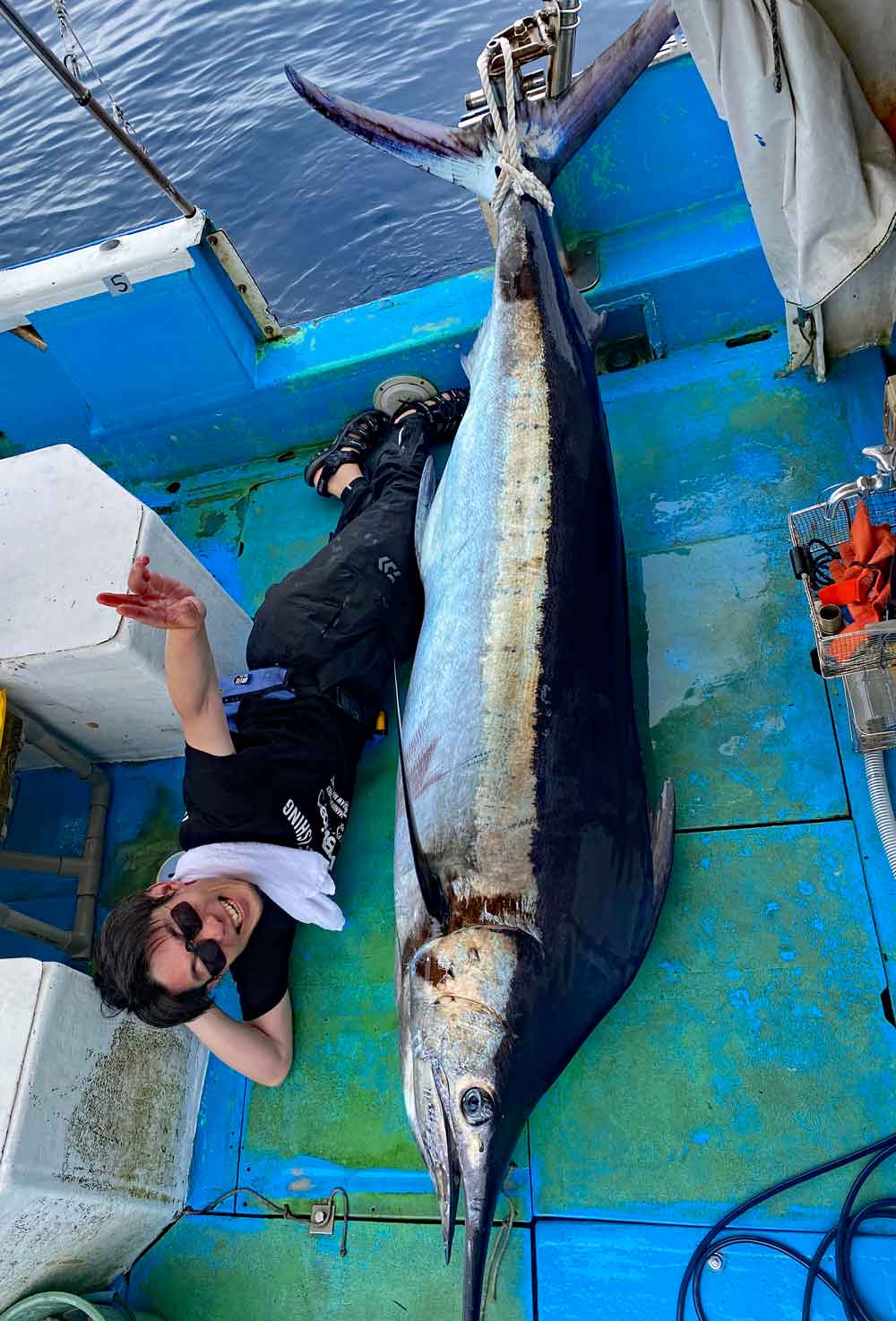 船に釣り上げたカジキと横になっている釣り師