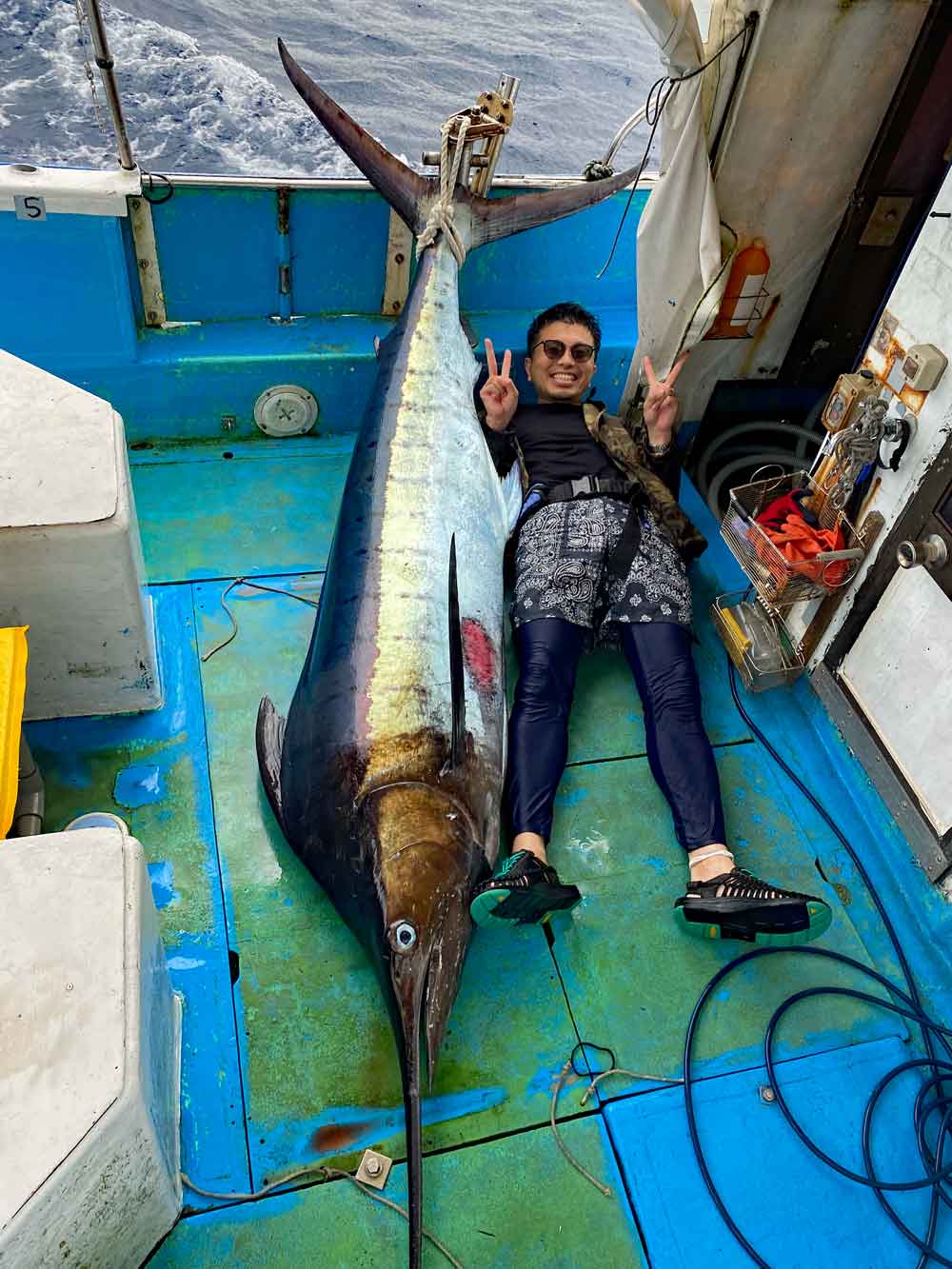 沖縄のトローリングで釣り上げたカジキとピースサインの男性