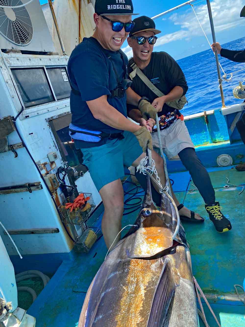 釣り上げたカジキを船に引き上げている二人の男性