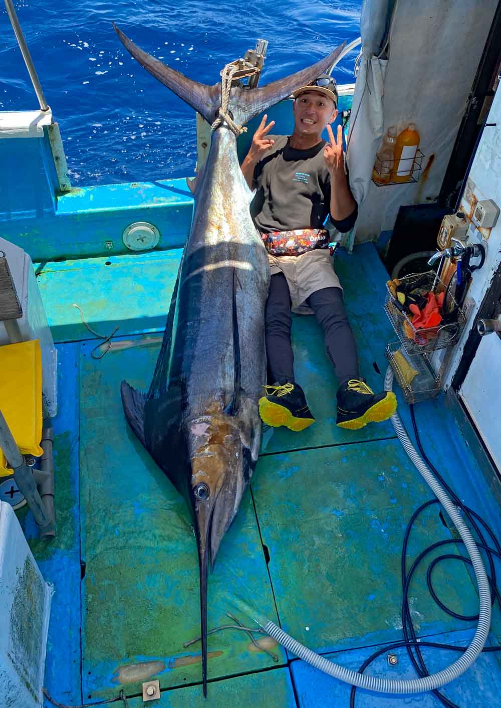 釣り上げたカジキとピースサインの男性