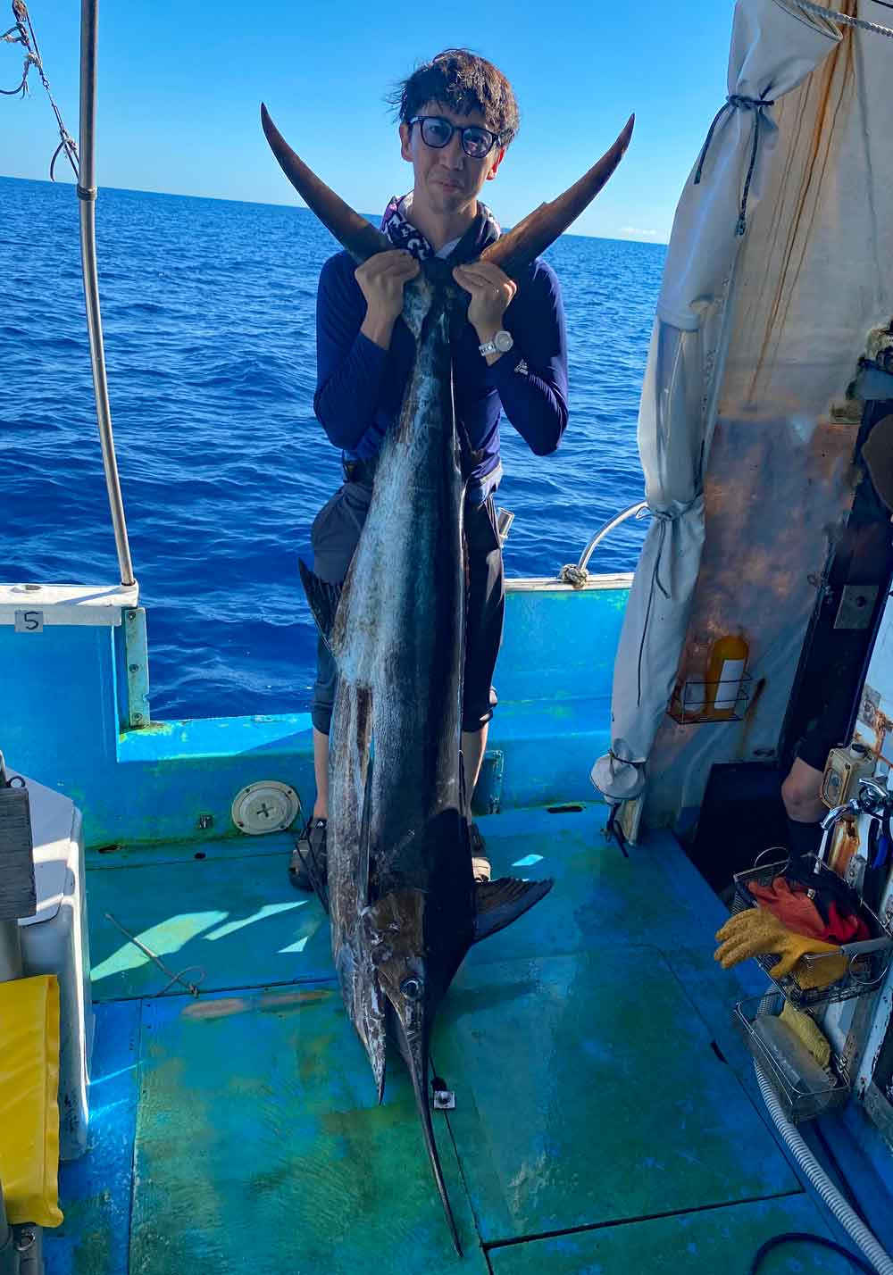 釣り上げたカジキの尾を持ち上げている男性