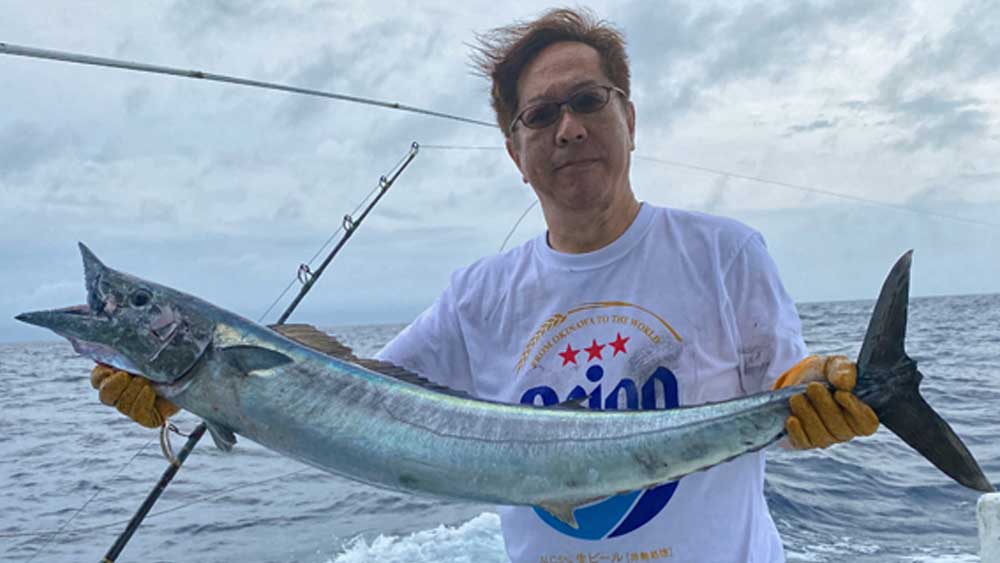 釣り上げたカマスサワラとオリオンビールのシャツの男性