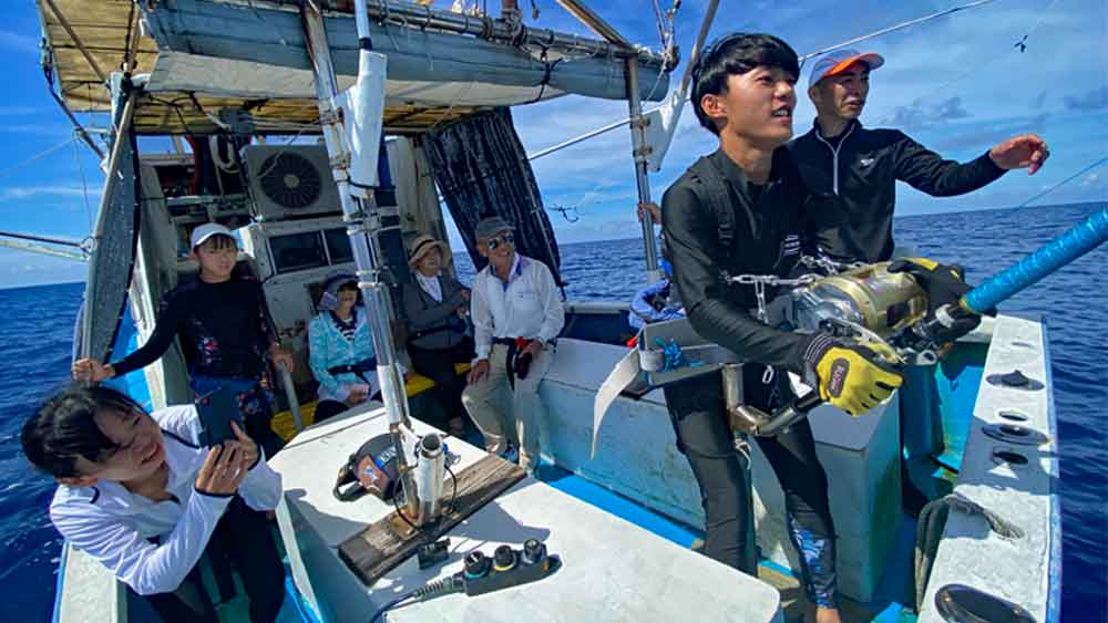 カジキ釣りをしている高校生と後ろで見守る家族