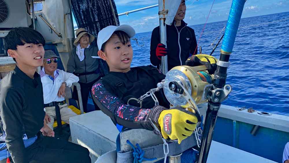 沖縄でカジキ釣りをしている女子中学生と後ろで見守る3世代の家族