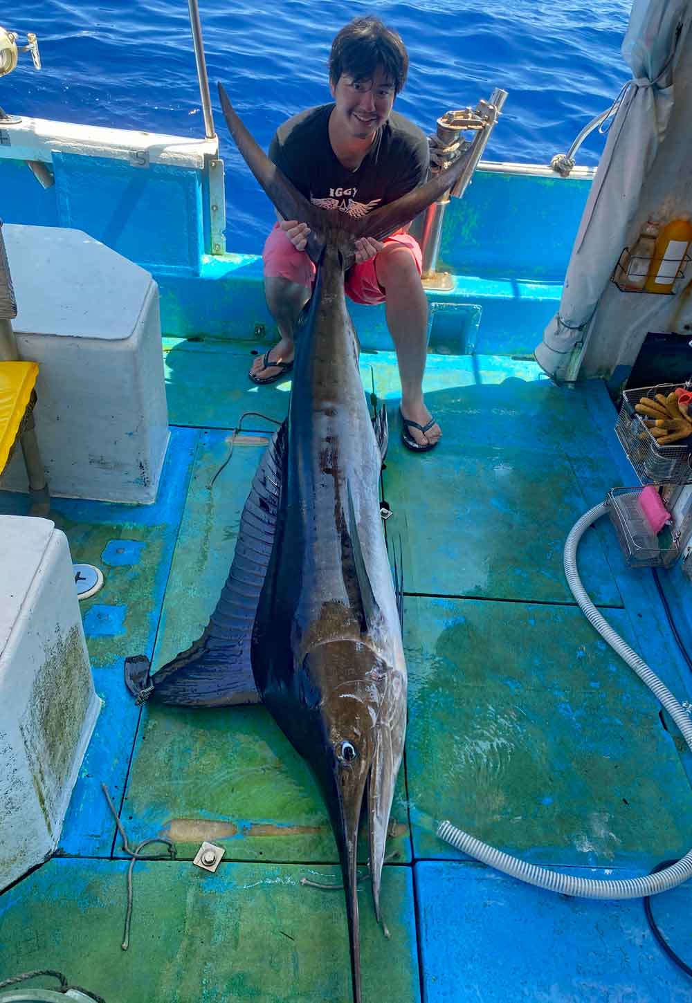 沖縄のトローリングで釣り上げたマカジキの尾を持っている男性