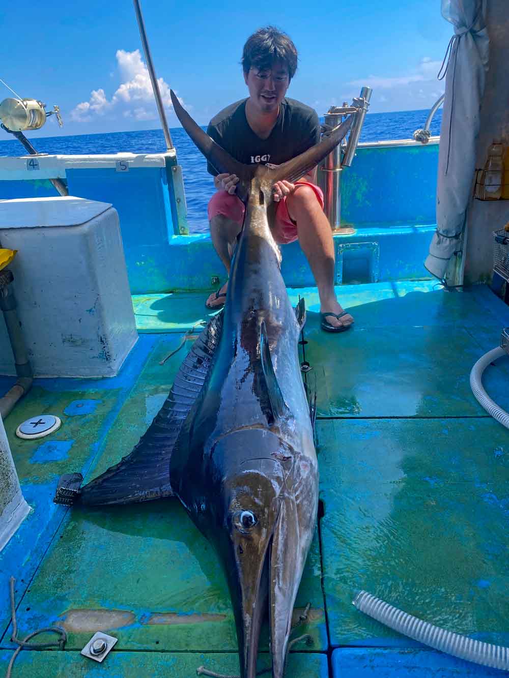 沖縄のトローリングで釣り上げたマカジキと尾を持ち上げている男性