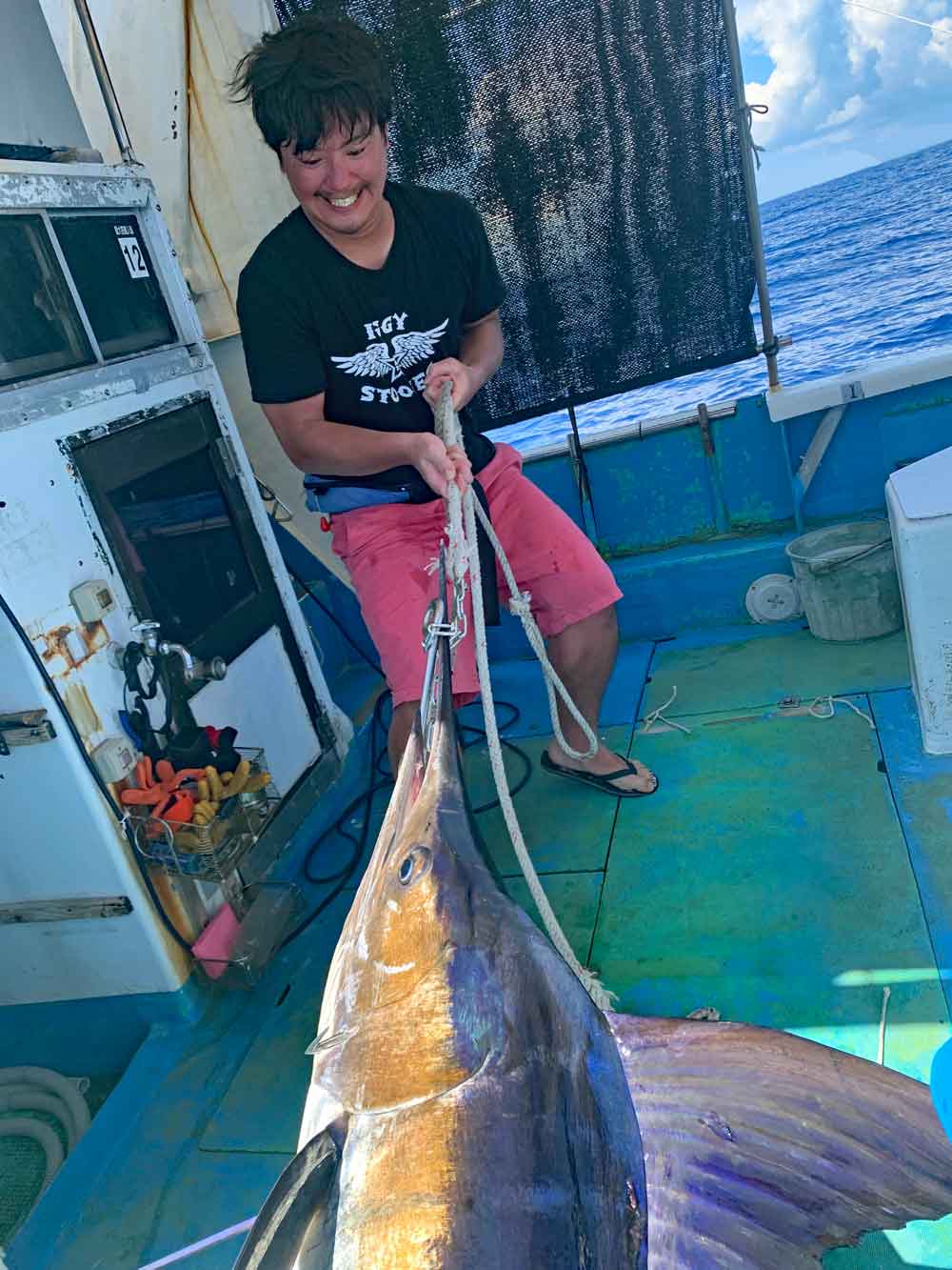 沖縄のトローリングで釣り上げたマカジキを船に引き上げている男性