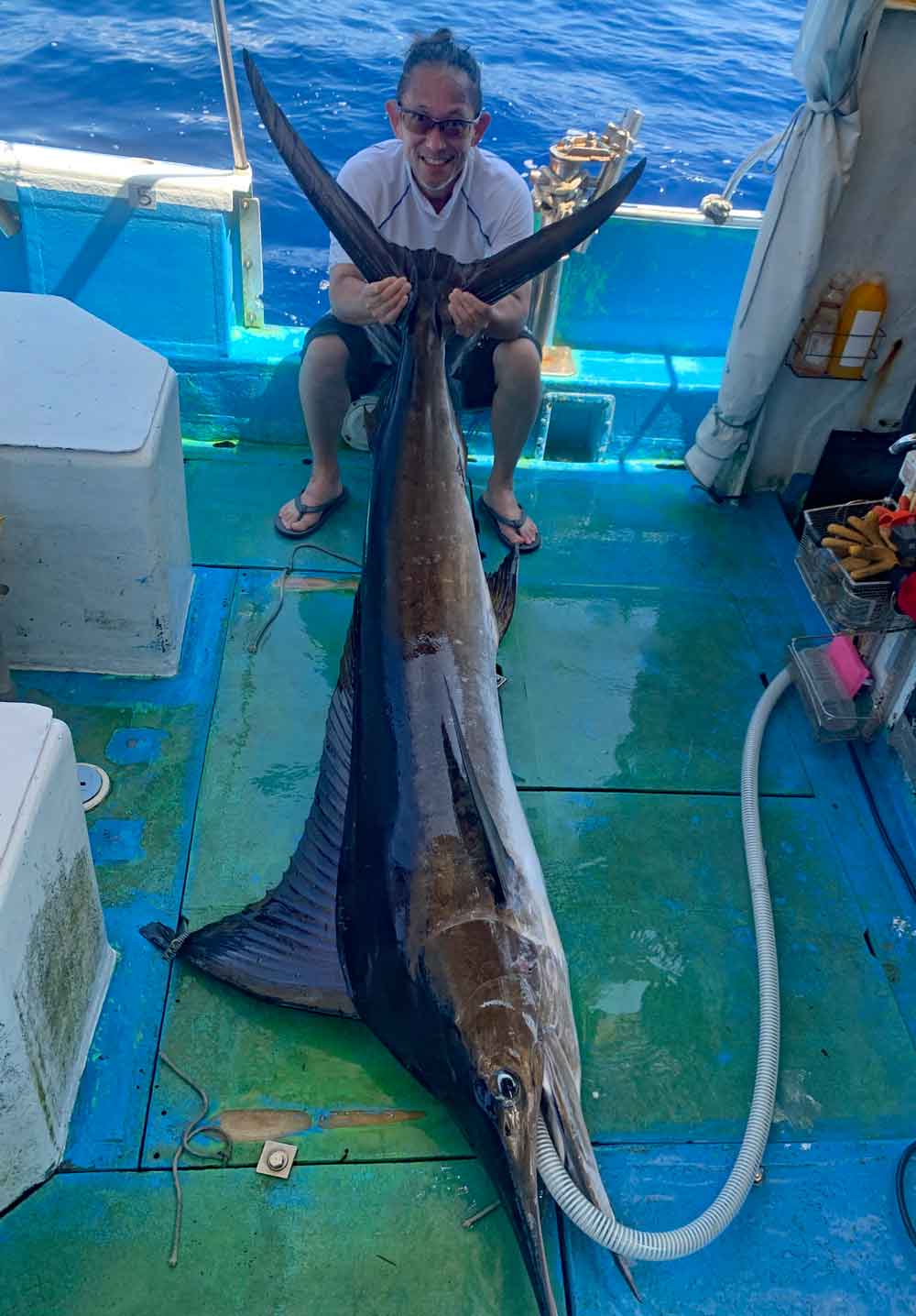 釣り上げたマカジキと尾を持ち上げている男性