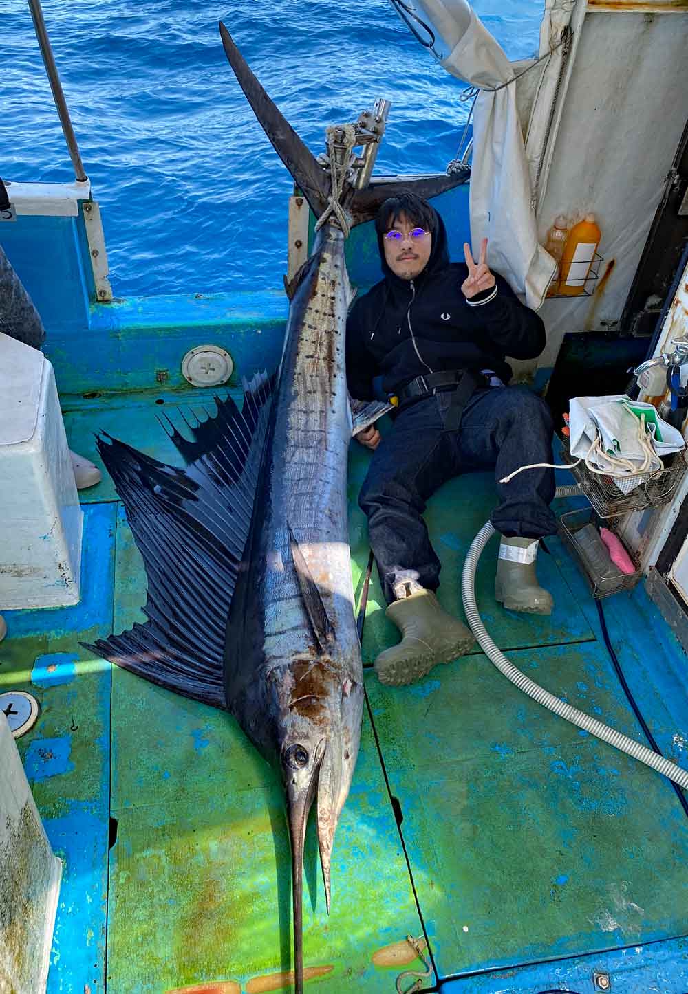 トローリングで釣り上げたバショウカジキとメガネをかけた釣り師