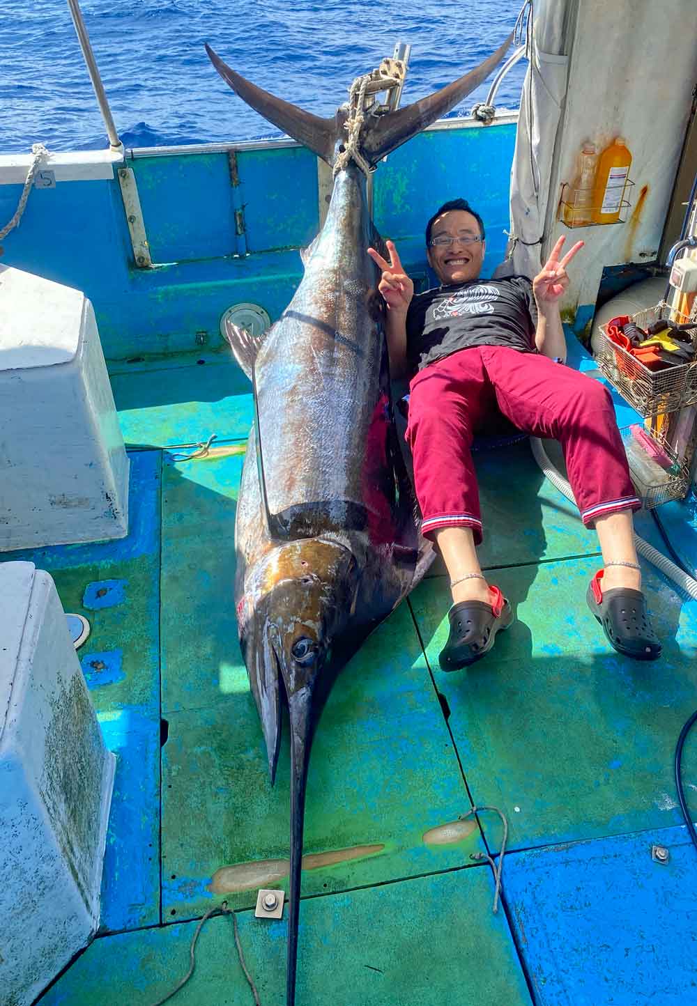 沖縄のトローリングでカジキを釣り上げ両手ピースの男性