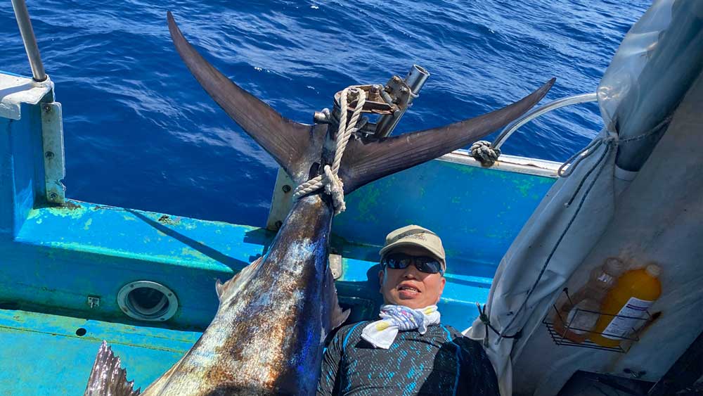 船に釣り上げたカジキの尾と男性