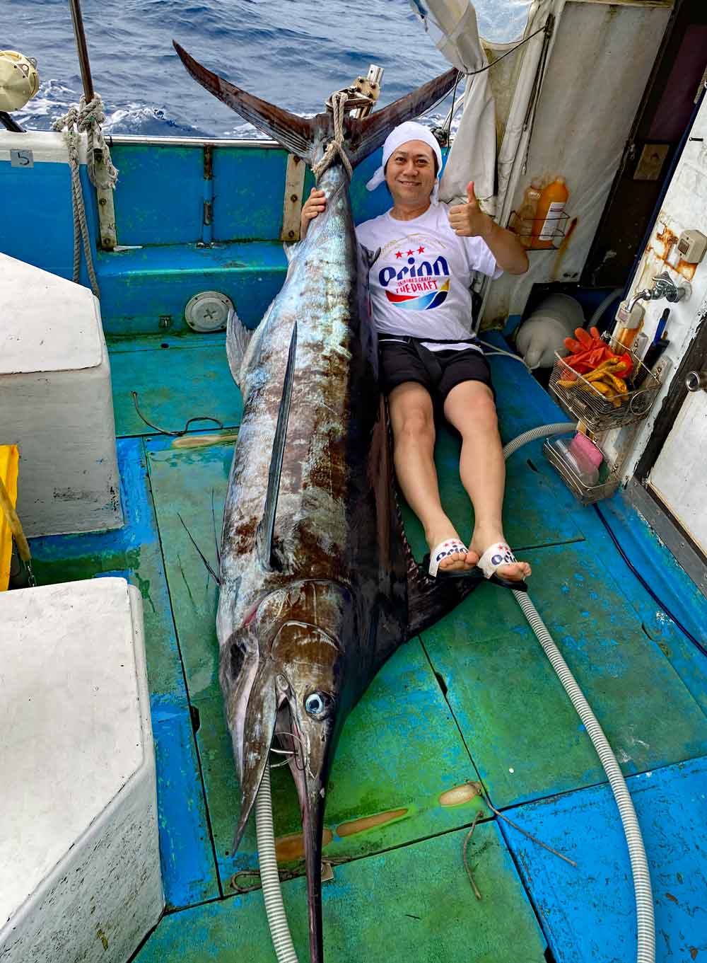 沖縄のトローリングでカジキを釣り上げ喜ぶオリオンビールシャツを着た男性