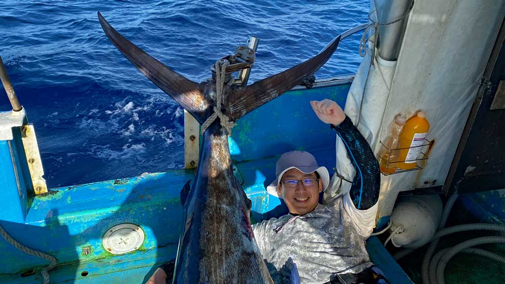 釣り上げたカジキの尾とガッツポーズの男性