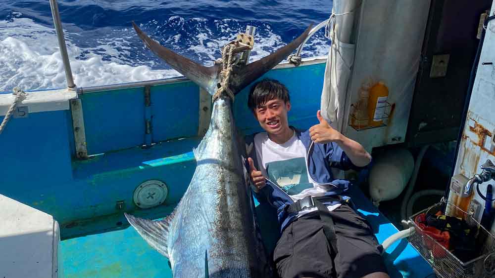 釣り上げたカジキの尾とガッツポーズの笑顔の男性