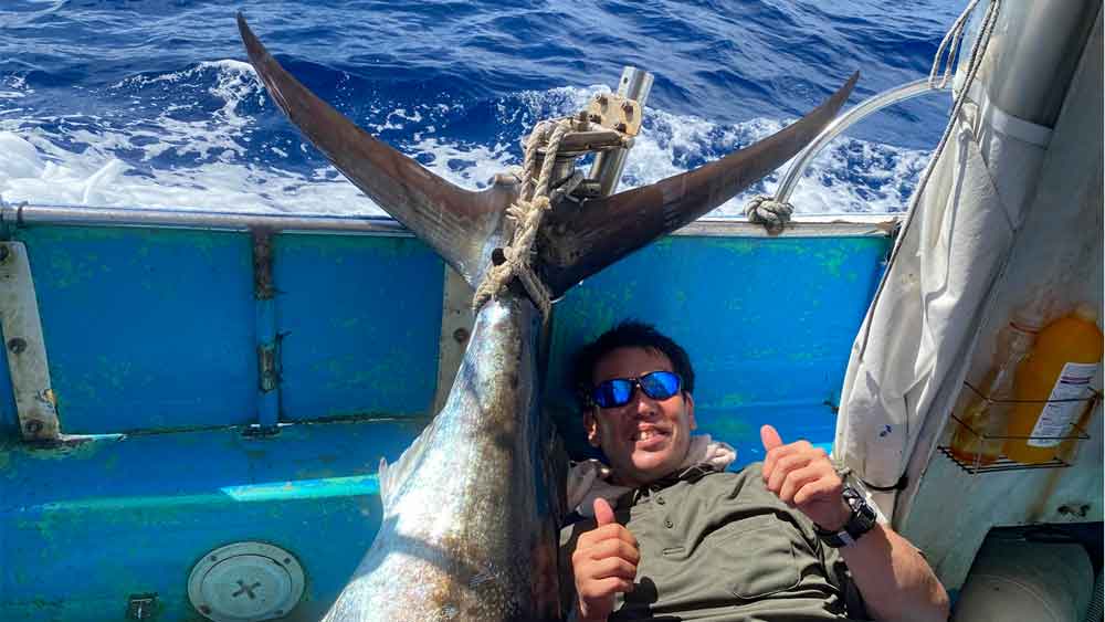 釣り上げたカジキの尾とガッツポーズの男性
