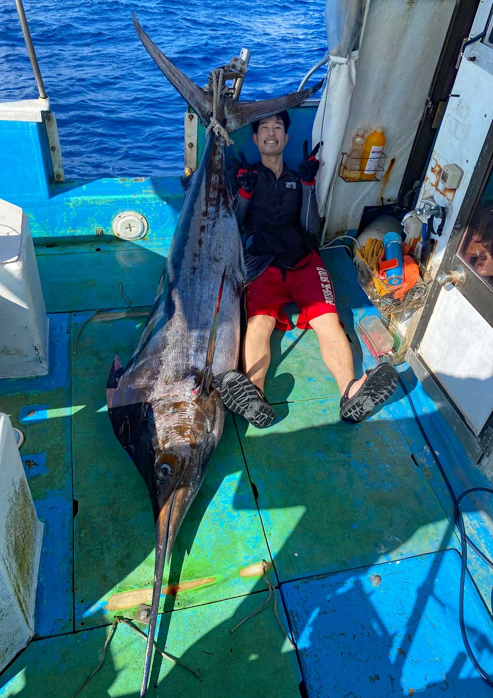 カジキを釣り上げピースサインで喜ぶ釣り師