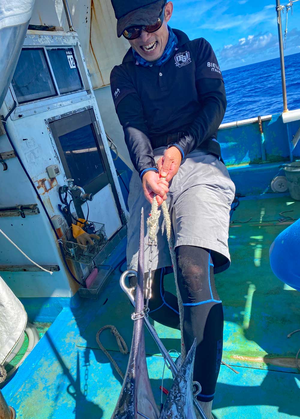 釣り上げたカジキを船に引き上げている男性