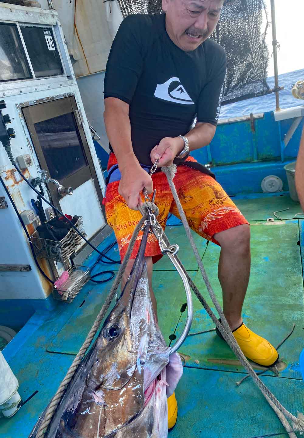 釣り上げたカジキを船に引き上げている男性