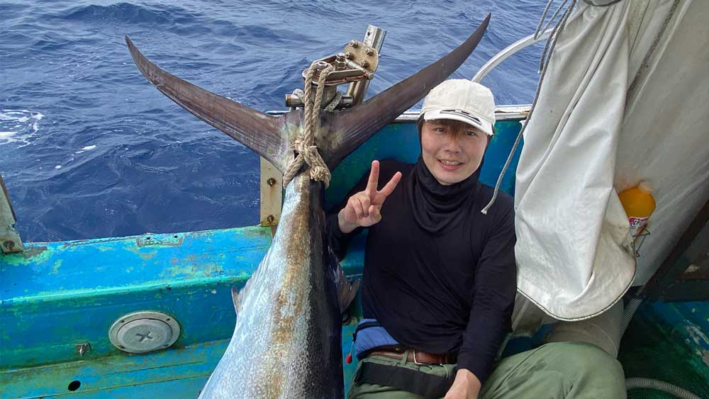 自ら釣り上げたカジキの尾と笑顔の男性