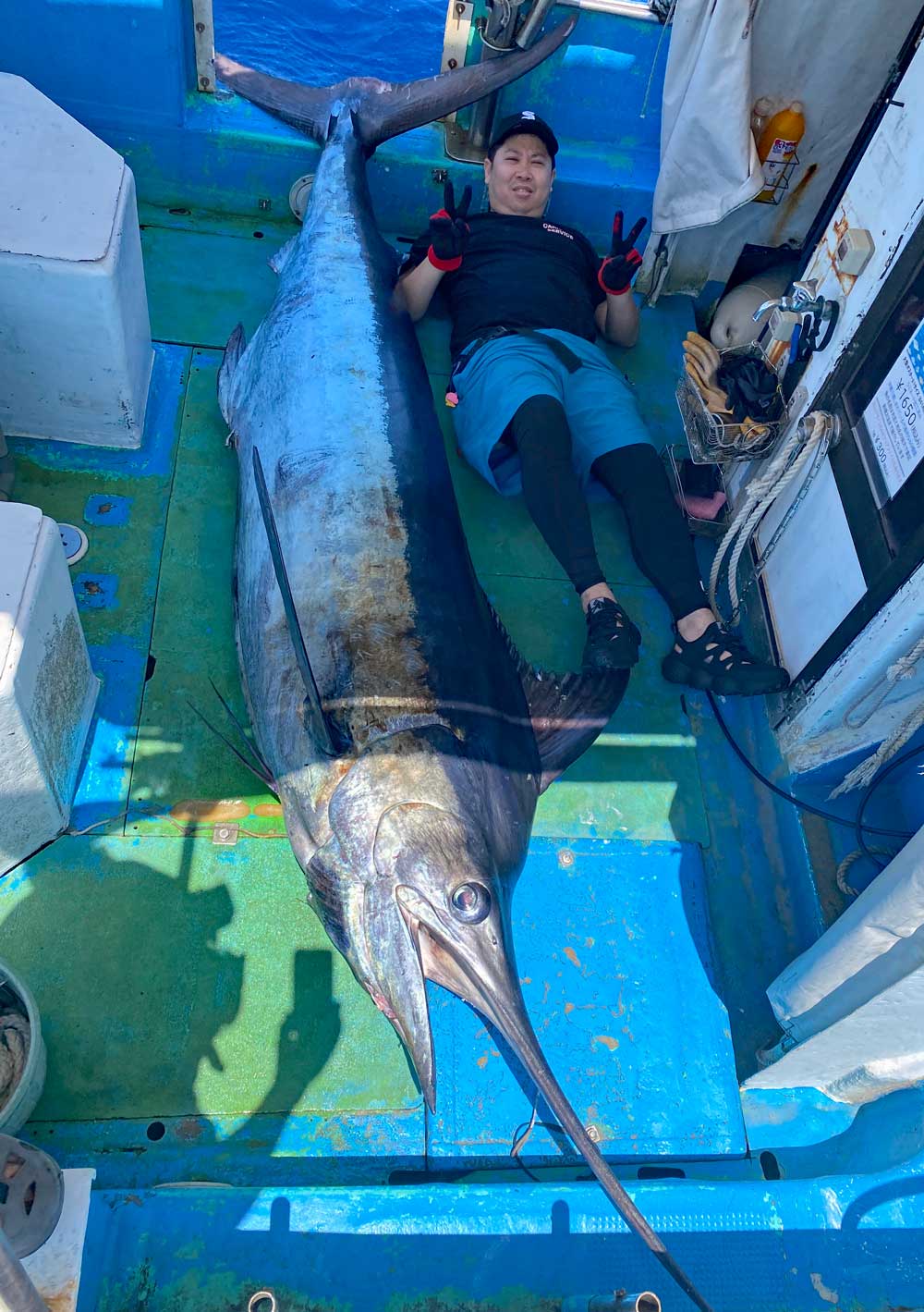 自ら釣り上げた180kgのカジキの横にピースサインの釣り師