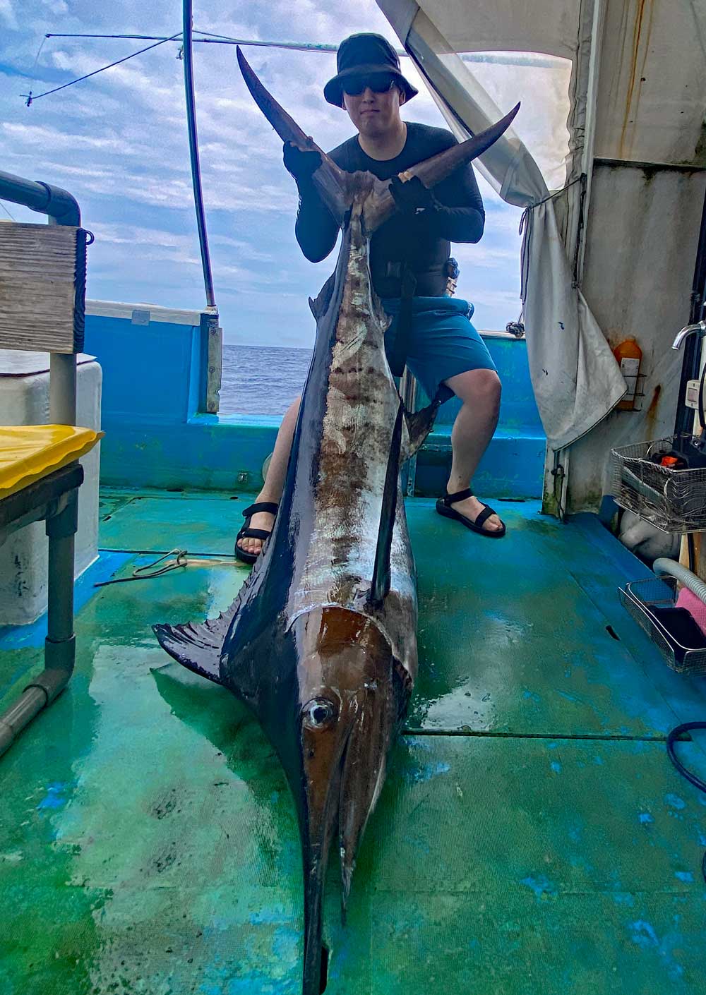 自ら釣り上げたカジキを尾を持ち上げている男性