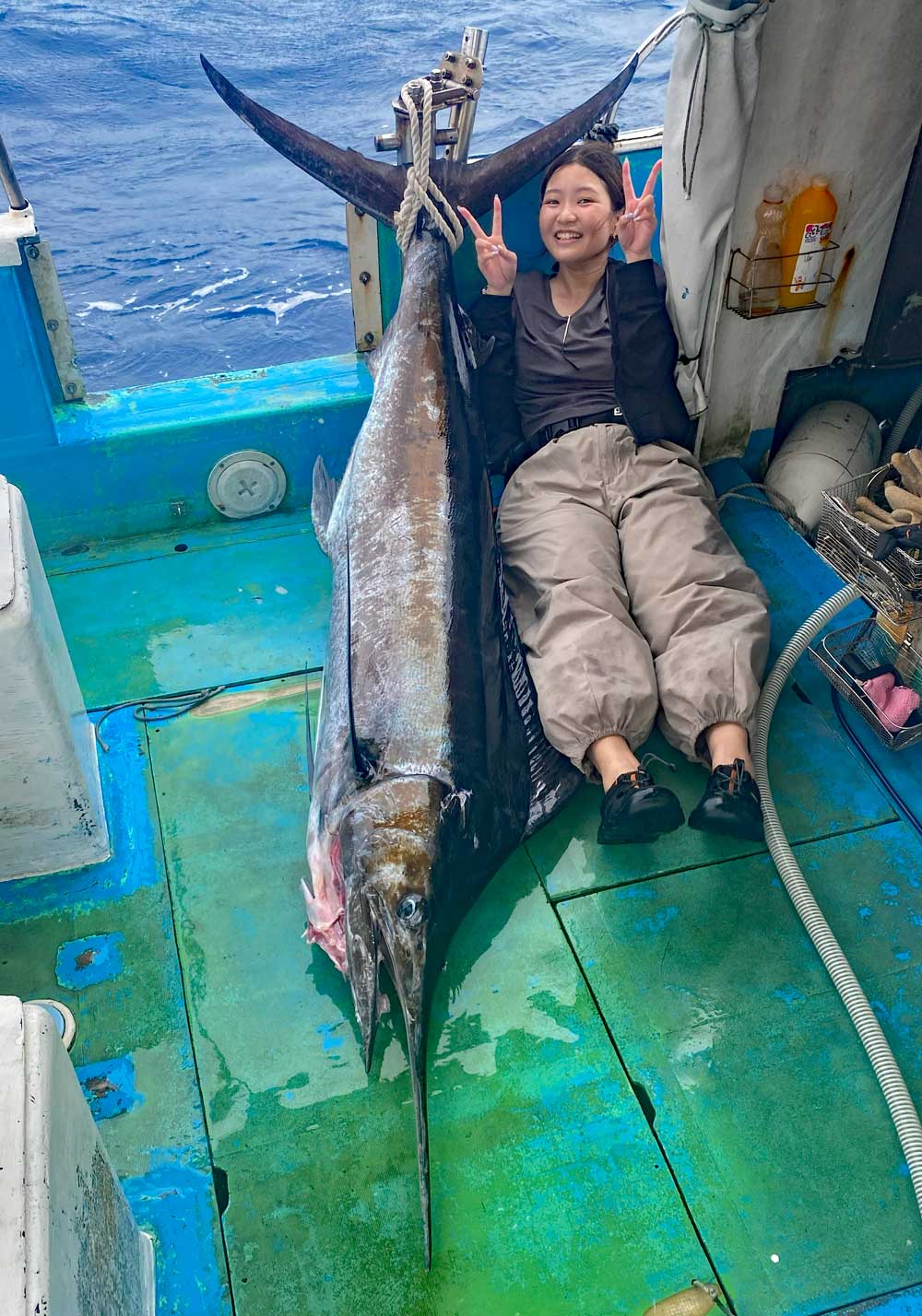 釣り上げたカジキとピースサインで笑顔の女性