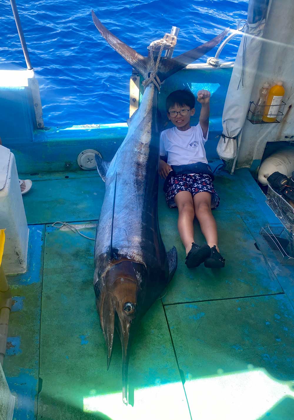 船のデッキに釣り上げたカジキと少年