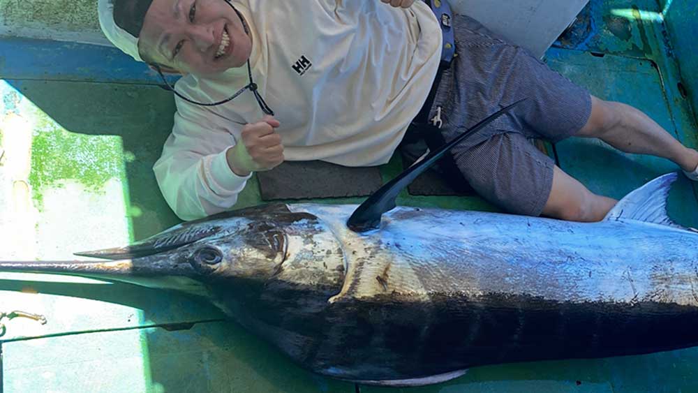 自ら釣り上げたカジキの横に笑顔の男性