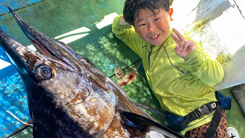 沖縄のトローリングで140kgのクロカジキ釣り上げピースサインの8才の小学3年生