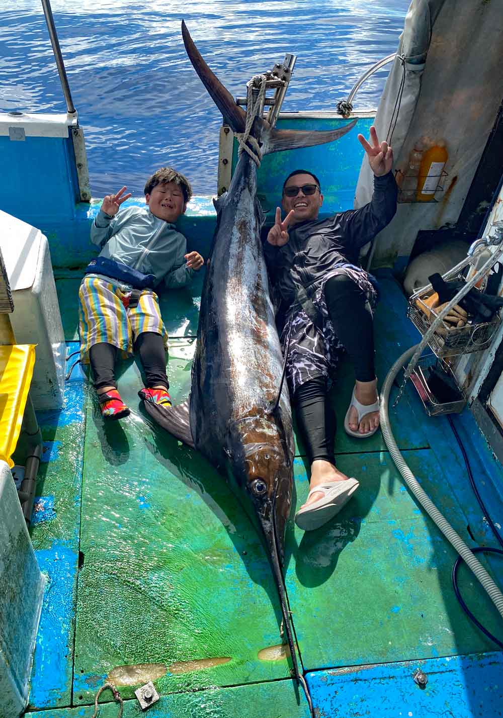 沖縄でカジキを釣り上げVサインで喜ぶ親子
