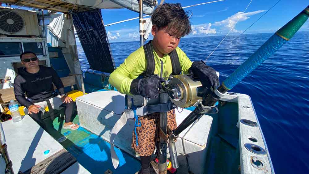 沖縄のトローリングで140kgのカジキ釣り上げグーサインの8才の小学3年生と後ろで見守る父
