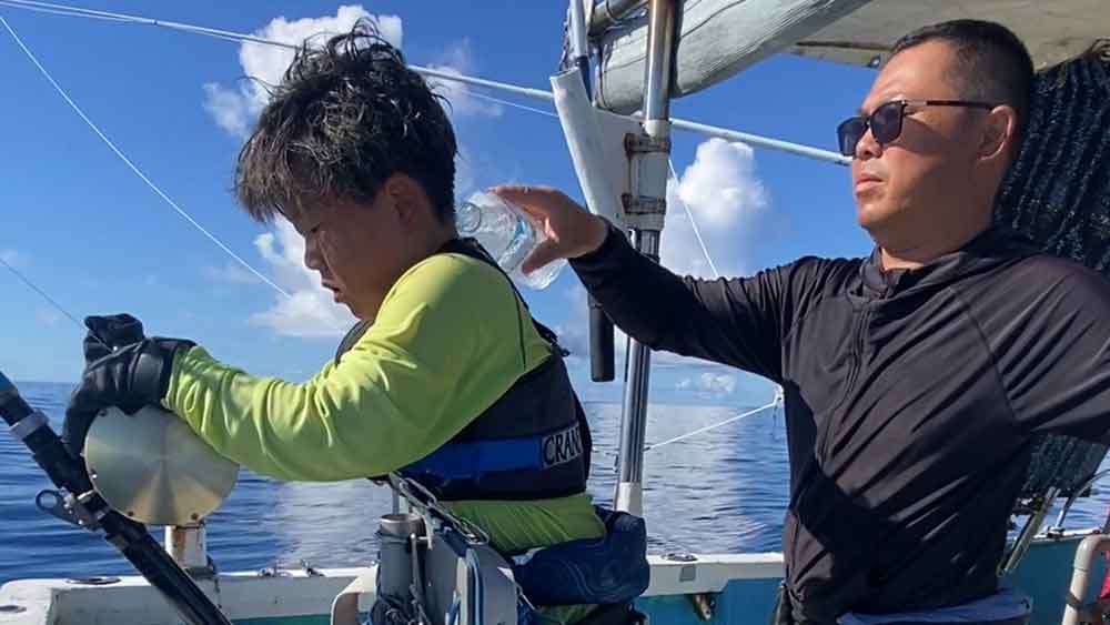 炎天下カジキ釣りをしている8才の小学生の後ろで水をかけようとしている父