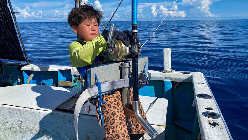 沖縄のトローリングでカジキ釣りで後に体をそらせる8才の小学3年生