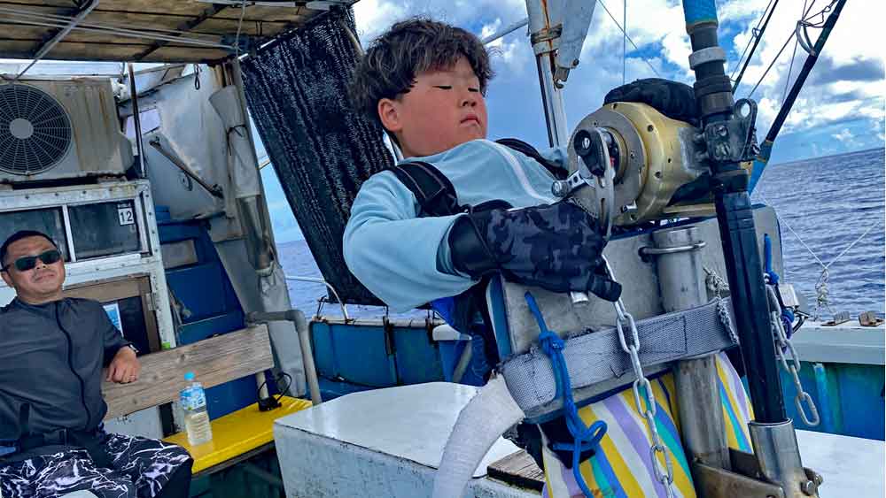 沖縄でカジキ釣りをしている８才の小学生3年生と後ろで見守る父
