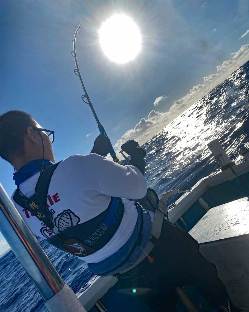 沖縄でカジキ釣りをしている男性の上に太陽