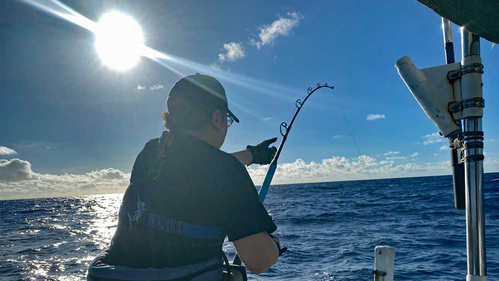 沖縄でカジキ釣りをしている男性の上に太陽