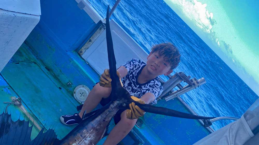 バショウカジキを釣り上げ尾を持ち上げている小学校4年生の少年