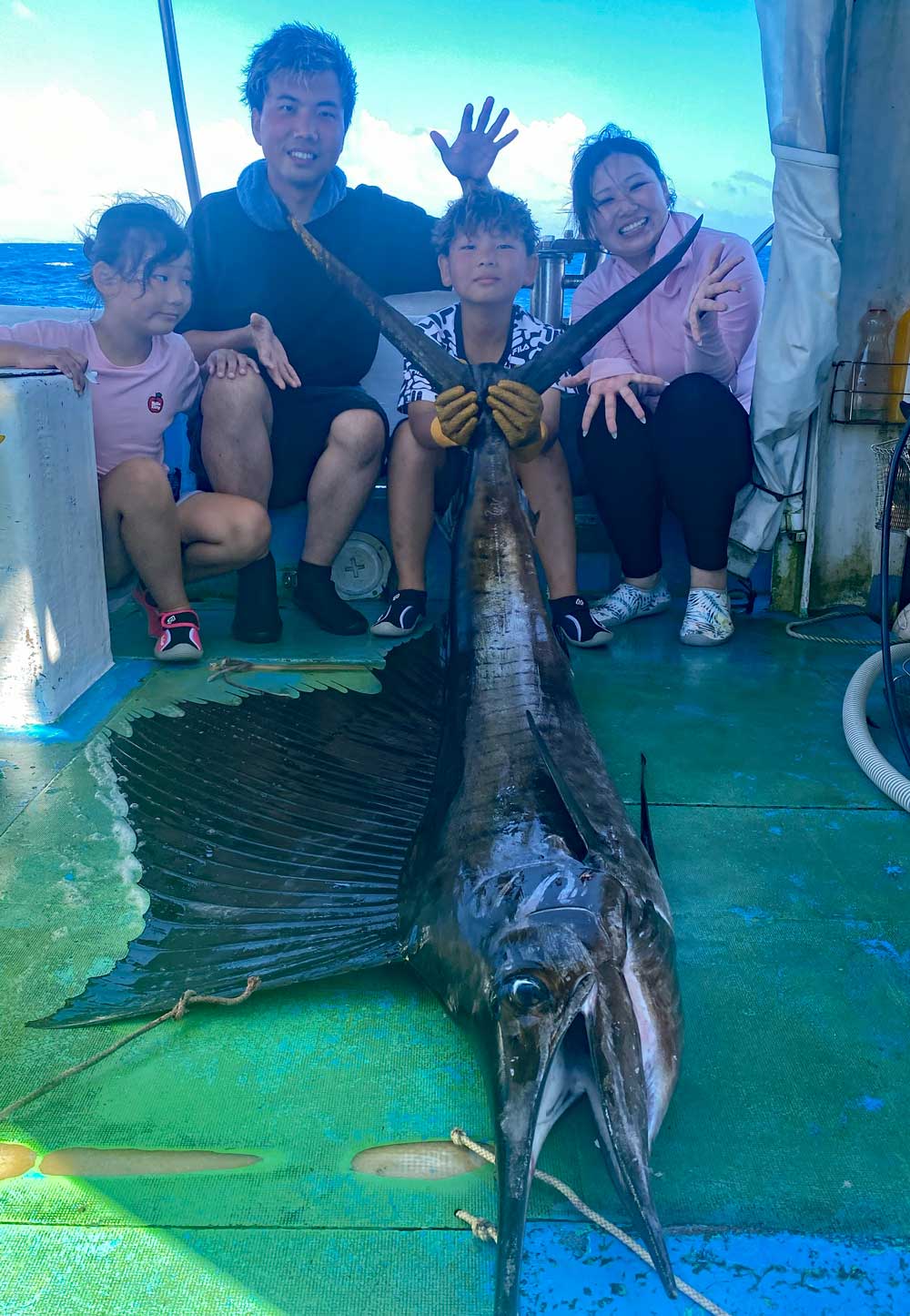 沖縄のトローリングでバショウカジキを釣り上げ尾を持ち上げている小学校4年生の少年と家族