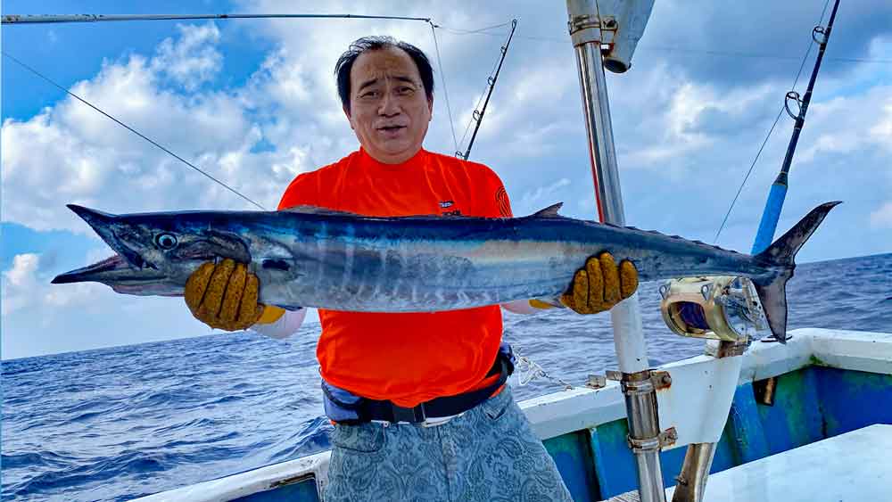 トローリングで大物カマスサワラを釣り上げたオレンジ色のシャツの男性